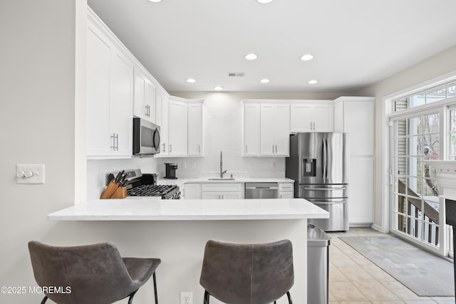 kitchen with stainless steel appliances, light countertops, visible vents, a sink, and a peninsula