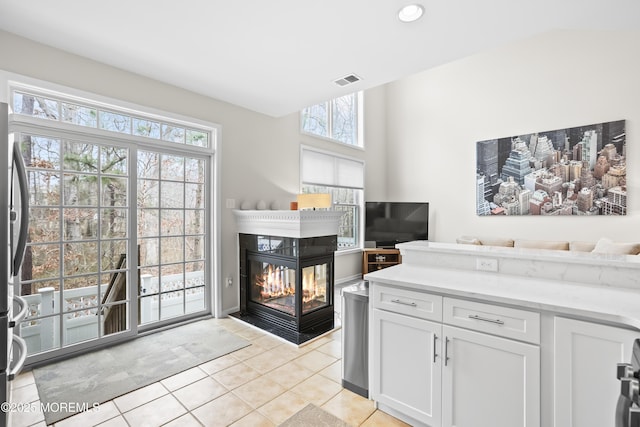 kitchen with light tile patterned floors, visible vents, white cabinets, freestanding refrigerator, and a multi sided fireplace