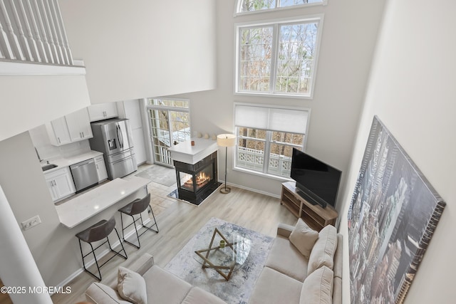 living room featuring baseboards, a multi sided fireplace, light wood finished floors, and a high ceiling