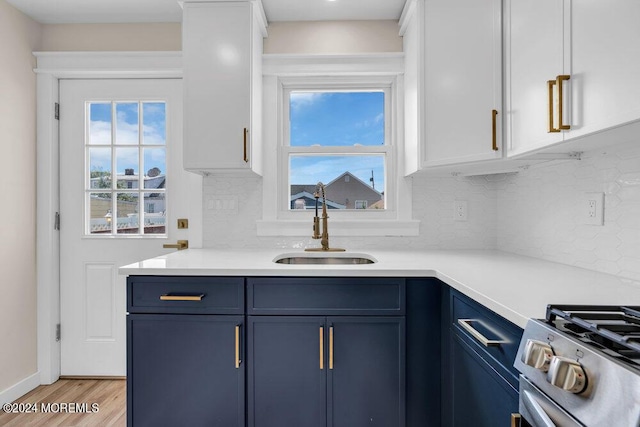 kitchen with stainless steel range with gas cooktop, light countertops, backsplash, a sink, and blue cabinets