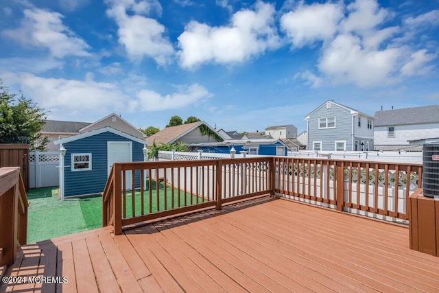 deck with a fenced backyard, a storage unit, a lawn, and an outdoor structure