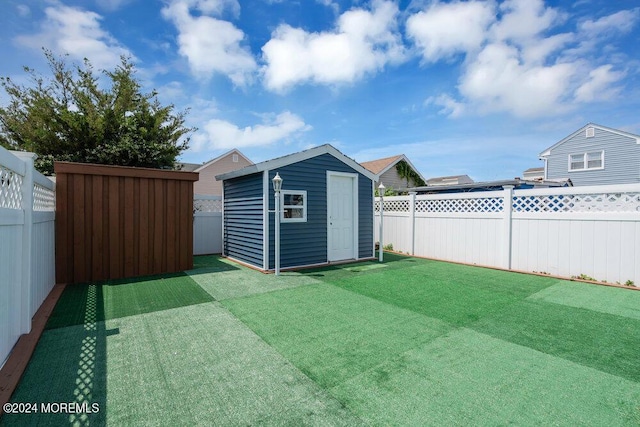 view of yard with a fenced backyard, a storage unit, and an outbuilding