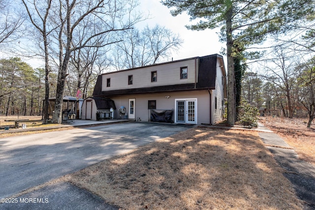 view of front of house with a gambrel roof, roof with shingles, an outbuilding, a storage unit, and french doors