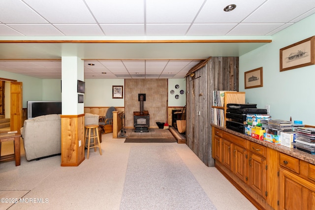 interior space with a wood stove, a drop ceiling, and a wainscoted wall