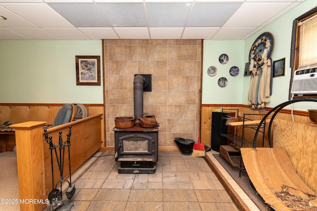 living room featuring a wood stove, a wainscoted wall, wood walls, and a drop ceiling