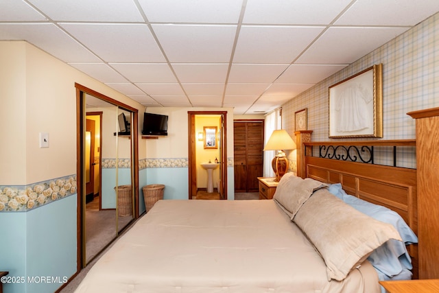 bedroom featuring a paneled ceiling, a closet, ensuite bathroom, a sink, and wallpapered walls