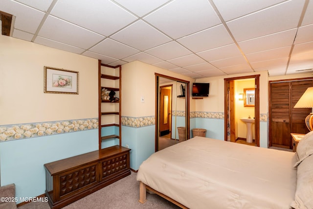 carpeted bedroom with ensuite bathroom, a closet, and a drop ceiling