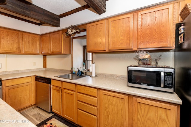 kitchen with beamed ceiling, stainless steel appliances, light countertops, light wood-type flooring, and a sink