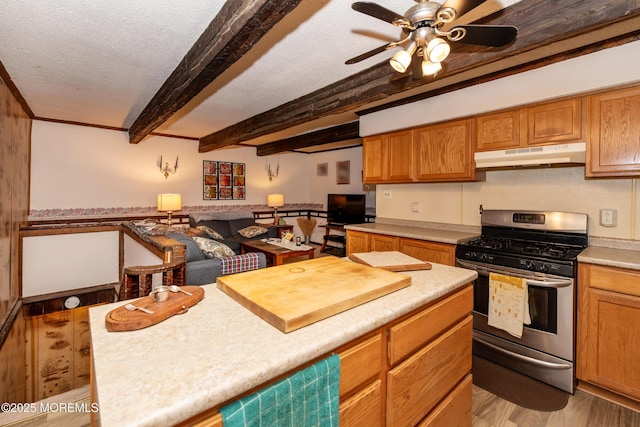 kitchen with a textured ceiling, under cabinet range hood, light countertops, beamed ceiling, and gas range