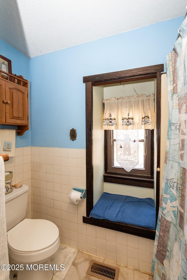 full bath featuring a textured ceiling, tile patterned flooring, toilet, visible vents, and tile walls