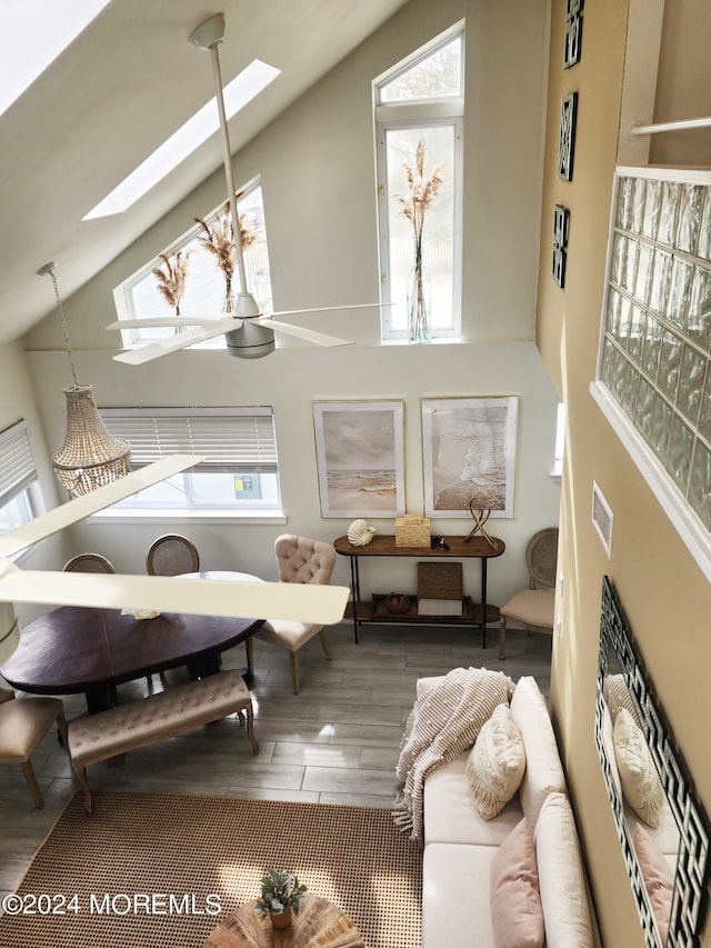 living room with high vaulted ceiling, a skylight, plenty of natural light, and wood finished floors