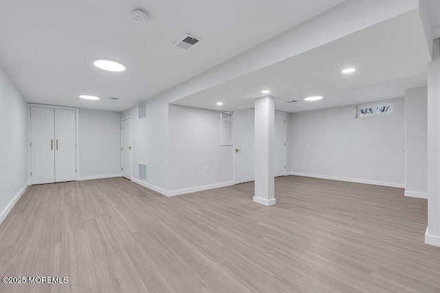 finished basement featuring visible vents, light wood-style flooring, and baseboards