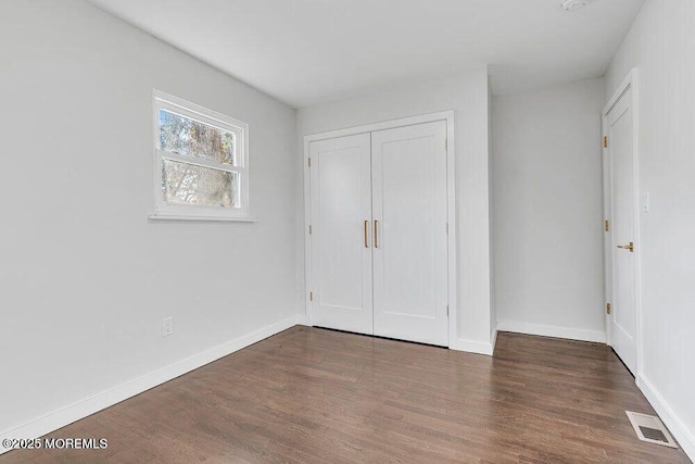 unfurnished bedroom with a closet, wood finished floors, visible vents, and baseboards