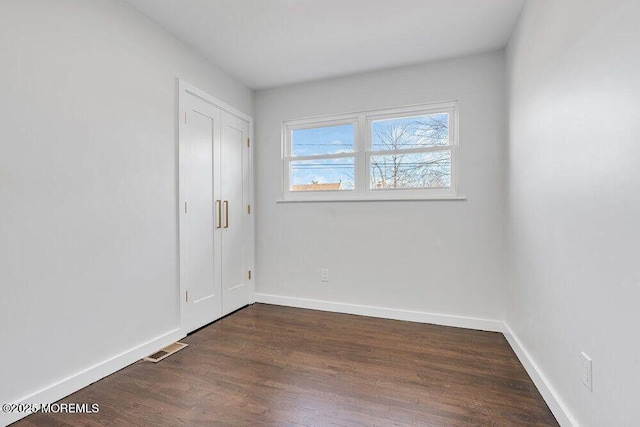 spare room featuring dark wood-style floors, visible vents, and baseboards