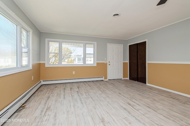 unfurnished room with a baseboard heating unit, wood finished floors, and visible vents