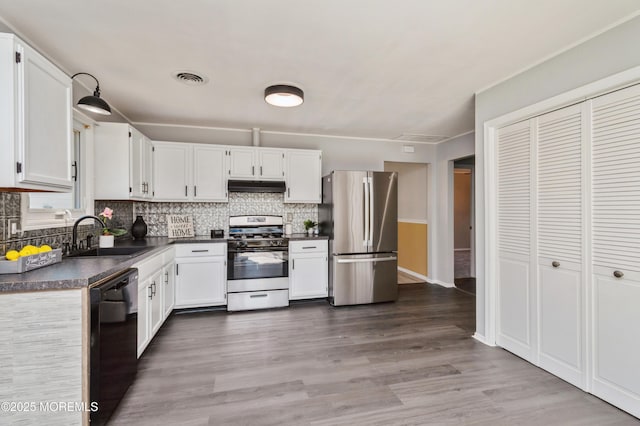 kitchen featuring visible vents, under cabinet range hood, a sink, dark countertops, and appliances with stainless steel finishes