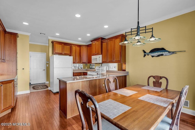 kitchen with visible vents, hardwood / wood-style floors, ornamental molding, a peninsula, and white appliances