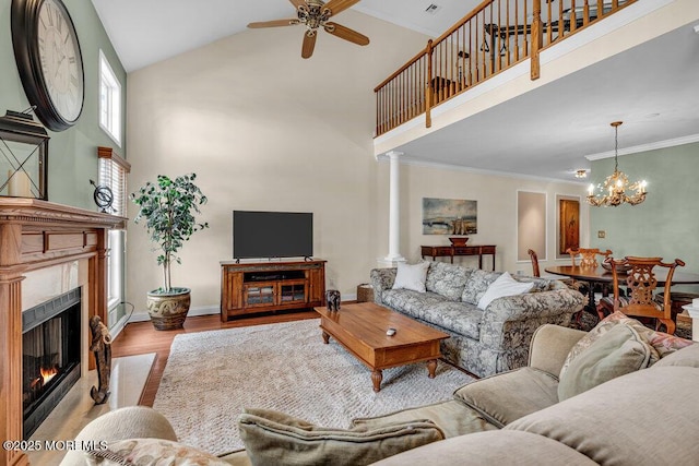 living area with wood finished floors, a high end fireplace, a towering ceiling, crown molding, and ceiling fan with notable chandelier