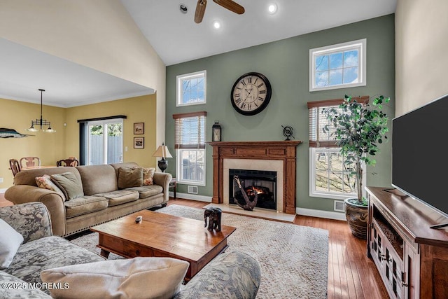 living room with high vaulted ceiling, a ceiling fan, hardwood / wood-style flooring, a lit fireplace, and baseboards