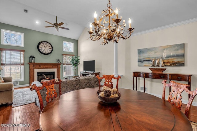 dining space featuring visible vents, vaulted ceiling, hardwood / wood-style floors, ceiling fan with notable chandelier, and a warm lit fireplace