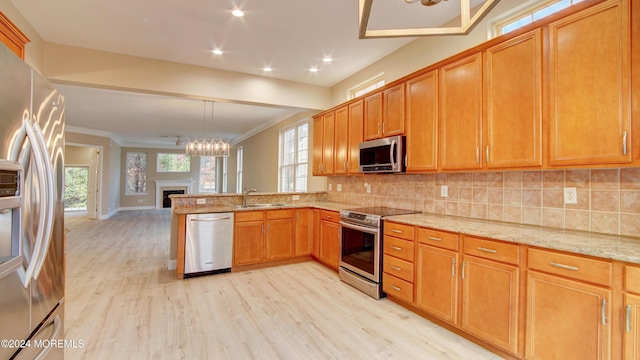 kitchen with light wood-style flooring, stainless steel appliances, a peninsula, a sink, and backsplash