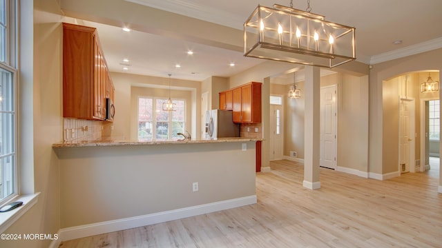 kitchen featuring arched walkways, light wood-style flooring, appliances with stainless steel finishes, brown cabinetry, and crown molding