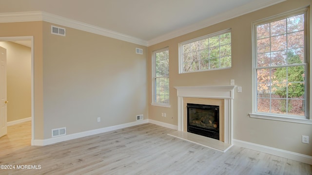 unfurnished living room with ornamental molding, a glass covered fireplace, visible vents, and wood finished floors