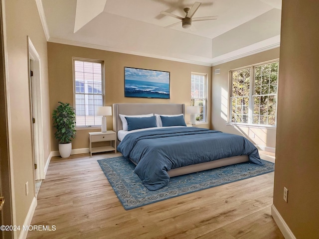 bedroom featuring baseboards, light wood finished floors, a raised ceiling, and crown molding