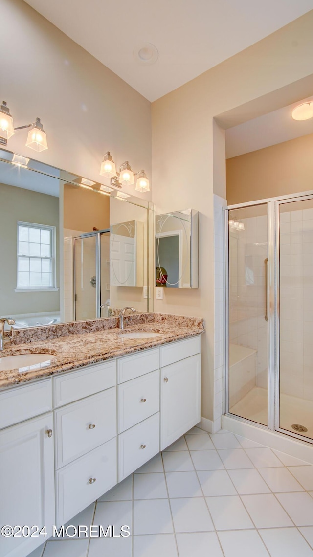 bathroom with double vanity, a shower stall, a sink, and tile patterned floors