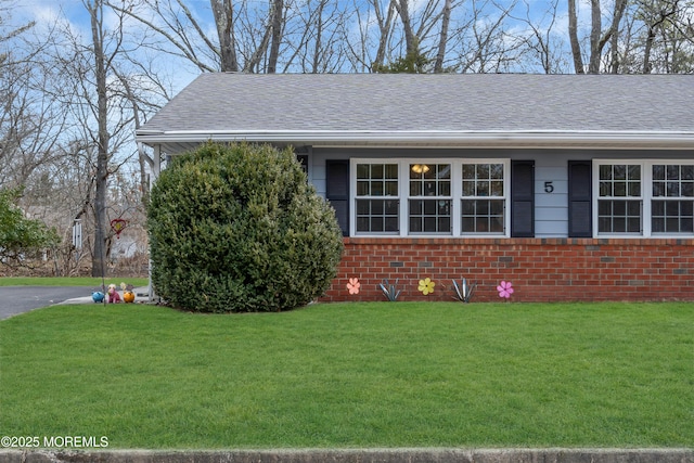 view of front of home with a shingled roof, brick siding, and a front lawn