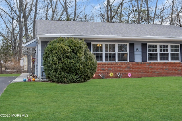 view of front of home with driveway, roof with shingles, a front yard, and brick siding