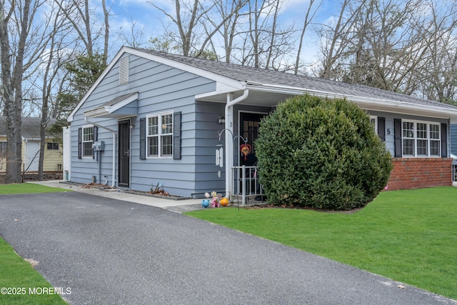 view of front of house with driveway, brick siding, a front yard, and a shingled roof