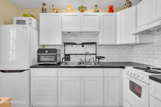 kitchen with dark countertops, white cabinetry, a sink, white appliances, and under cabinet range hood