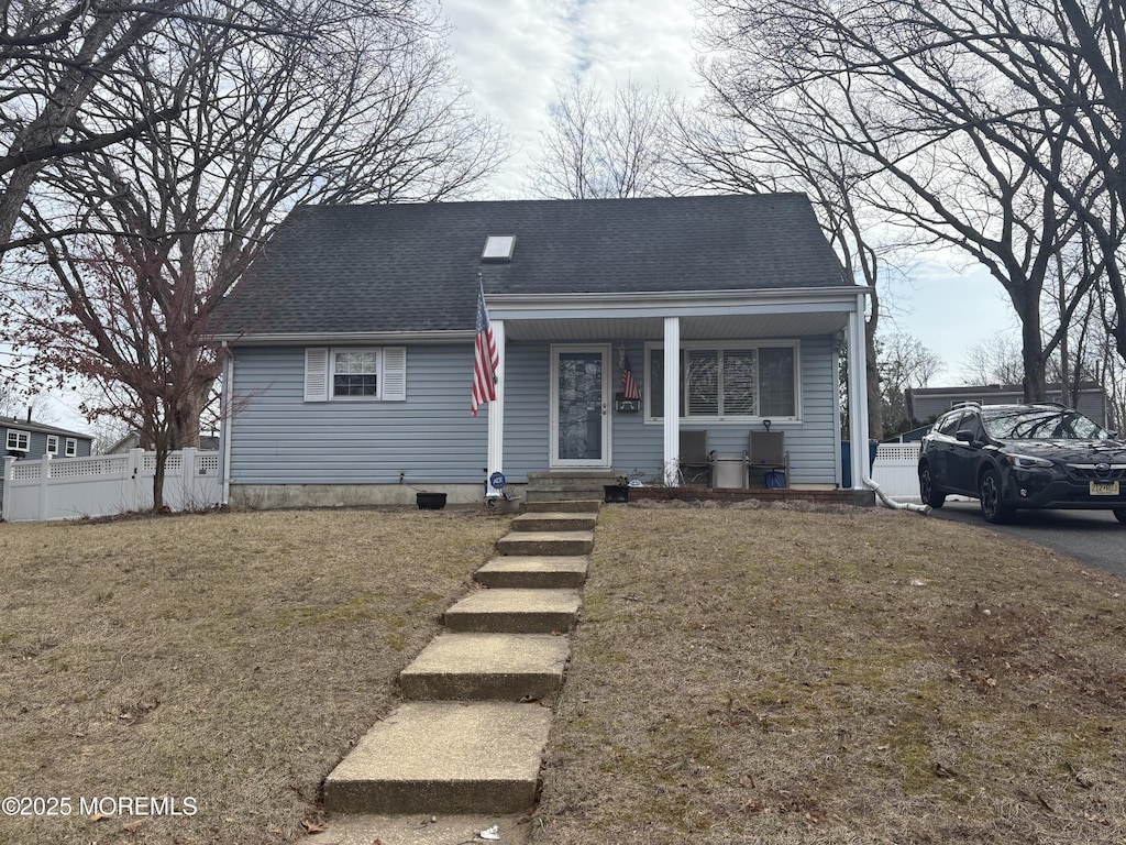 bungalow-style home with covered porch, fence, a front lawn, and roof with shingles