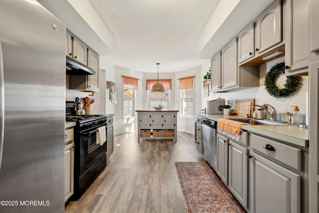 kitchen featuring under cabinet range hood, stainless steel appliances, light wood-style floors, a textured ceiling, and a sink