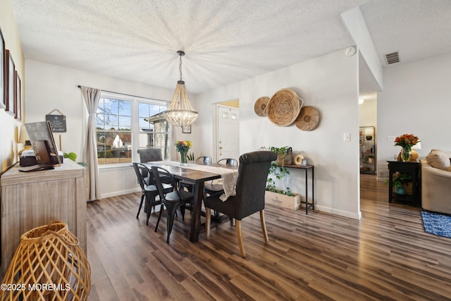 dining space featuring a notable chandelier, visible vents, a textured ceiling, and wood finished floors