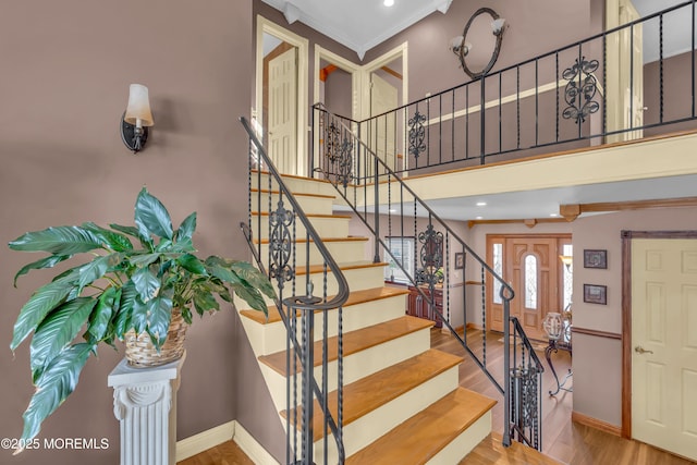 stairway with baseboards, a high ceiling, wood finished floors, and crown molding