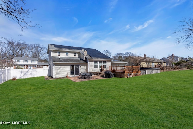 rear view of house featuring a deck, roof mounted solar panels, a fenced backyard, a yard, and a patio area