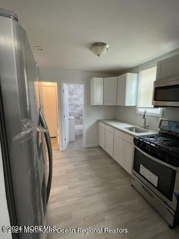 kitchen with light wood finished floors, light countertops, appliances with stainless steel finishes, white cabinets, and a sink