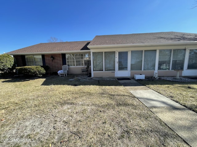 ranch-style house with a sunroom, brick siding, a front lawn, and roof with shingles