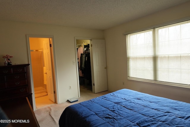 bedroom with connected bathroom, a spacious closet, a textured ceiling, and light colored carpet