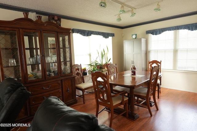 dining area with a textured ceiling, ornamental molding, and wood finished floors