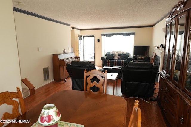 dining area featuring a textured ceiling, ornamental molding, wood finished floors, and visible vents