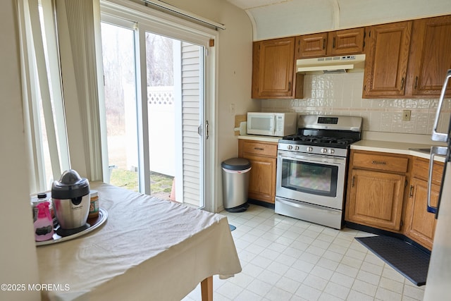 kitchen featuring stainless steel gas range oven, decorative backsplash, white microwave, light countertops, and under cabinet range hood