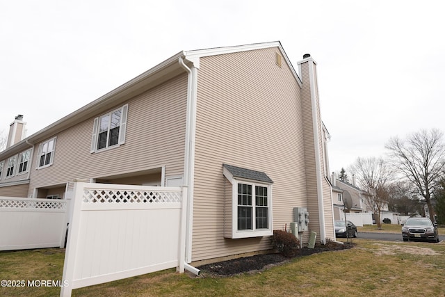 view of home's exterior featuring a chimney, fence, and a lawn