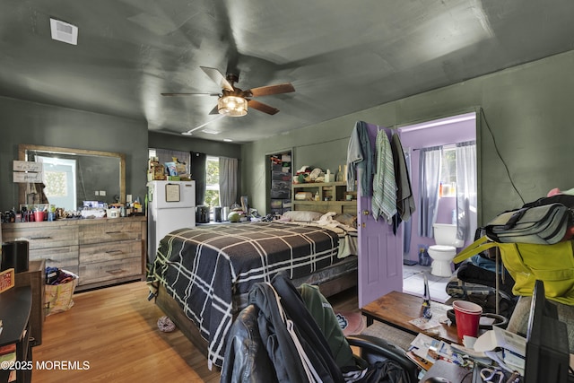 bedroom featuring visible vents, connected bathroom, ceiling fan, freestanding refrigerator, and light wood-style floors