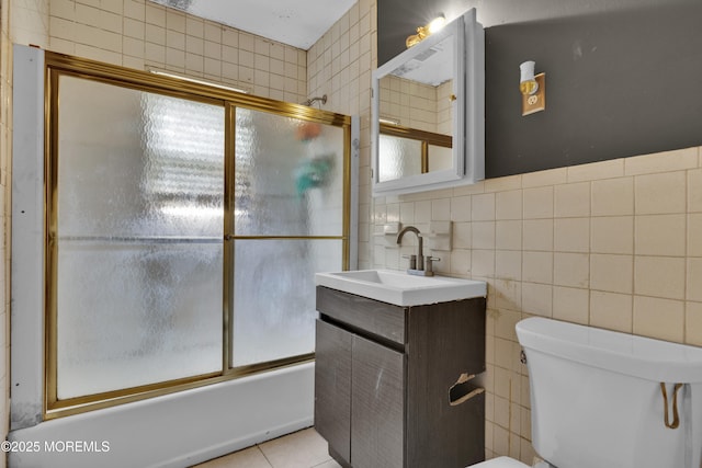 full bath with toilet, tile patterned floors, combined bath / shower with glass door, vanity, and tile walls