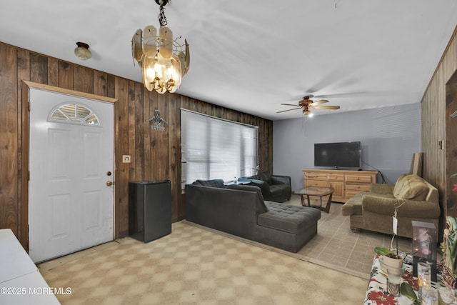 living room with ceiling fan with notable chandelier, light floors, and wood walls