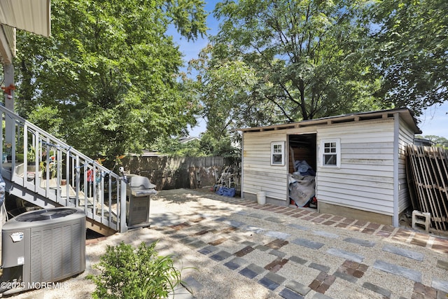 view of patio / terrace featuring an outbuilding, central air condition unit, area for grilling, fence, and a storage unit