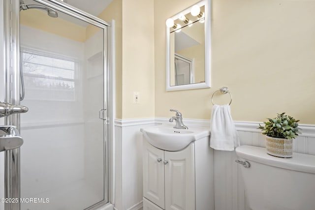 bathroom featuring vanity, a stall shower, wainscoting, a decorative wall, and toilet